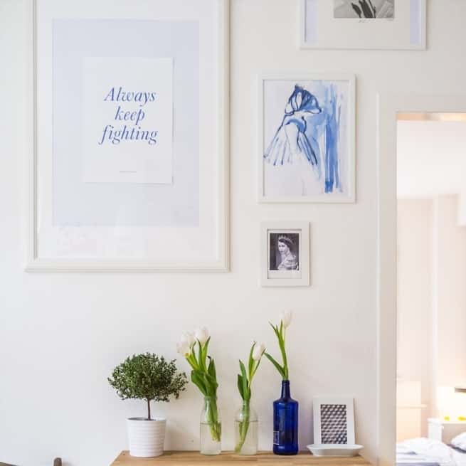 spring gallery wall inspo with blue artwork, and fresh flowers in vases below