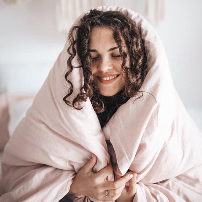 Smiling girl with curly hair with a pink duvet wrapped around her head practicing self love